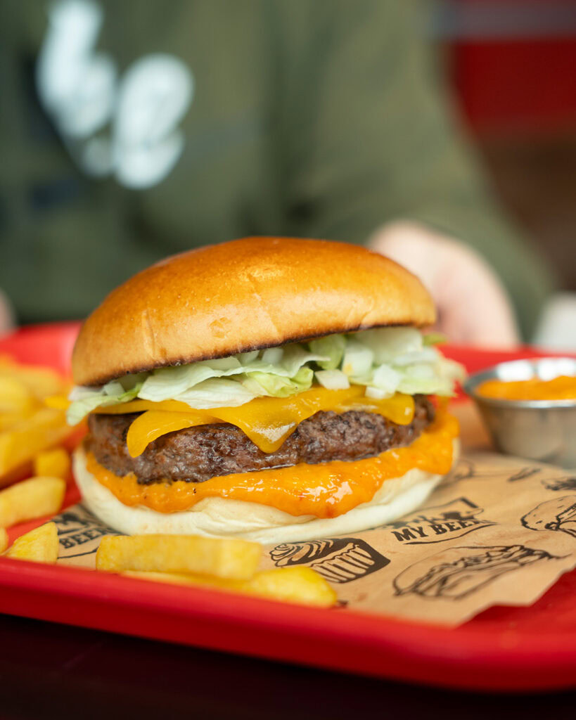 Burger épicé avec fromage, légumes frais et sauce piquante, présenté sur un plateau rouge.